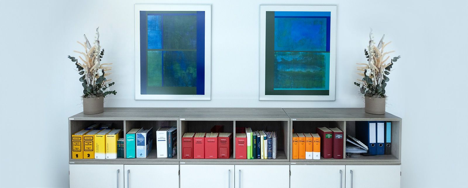 Sideboard mit Büchern und darüber 2 abstrakte Gemälde.