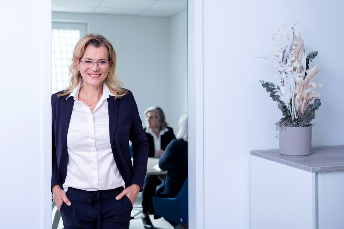 Steuerberaterin im Business-Outfit lächelt am Eingang eines Besprechungsraums